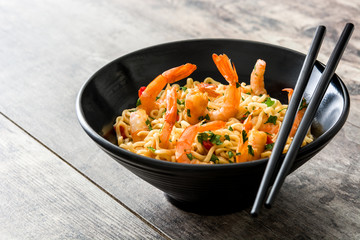 Noodles and shrimps with vegetables in black bowl on wooden table
