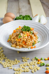 Fried macaroni with egg and pork and vegetable in tomato sauce in plate on a wooden table.