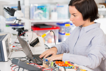 Female laboratory assistant Repairs PCB module for CNC robotics. Measurement of the parameters of the electronic system in the laboratory