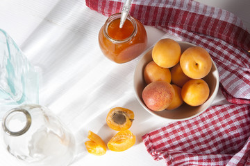the Apricots in a bowl and jam in a jar on a white table with a red and white towel, handmade summer blanks