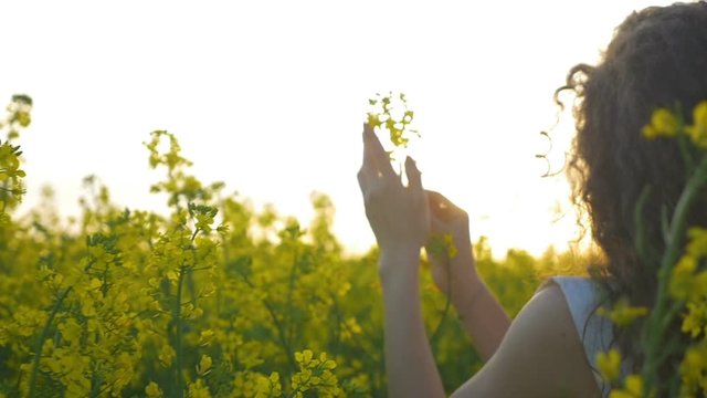 Slow motion of country girl gracefully touching a rapeseed flower standing on the meadow