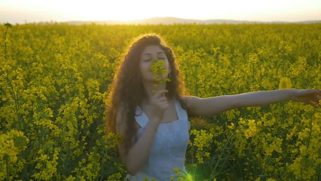Slow motion of young woman with white dress dancing in the field full of canola flowers overwhelmed with the smell of nature