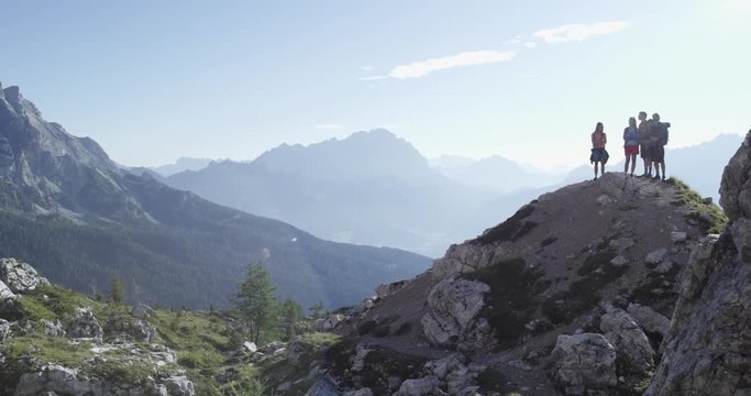 Four friends looking panorama on peak top hiking trail path. Group of friends people summer adventure journey in mountain nature outdoors. Travel exploring Alps, Dolomites. 4k slow motion 60p video