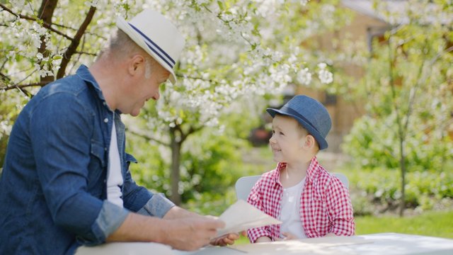 Granddad and his grandson are making wooden plane in the backyard on summertime