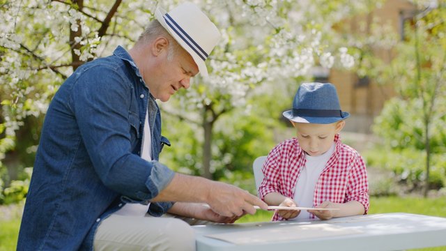 Granddad and his grandson are making wooden plane in the backyard on summertime