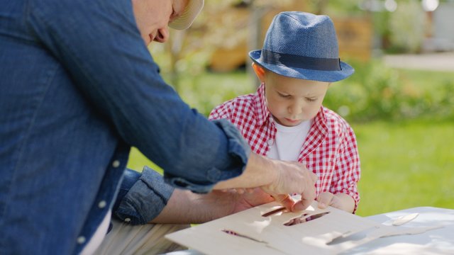 Granddad and his grandson are making wooden plane in the backyard on summertime