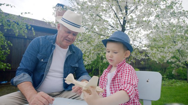Granddad and his grandson are making wooden plane in the backyard on summertime
