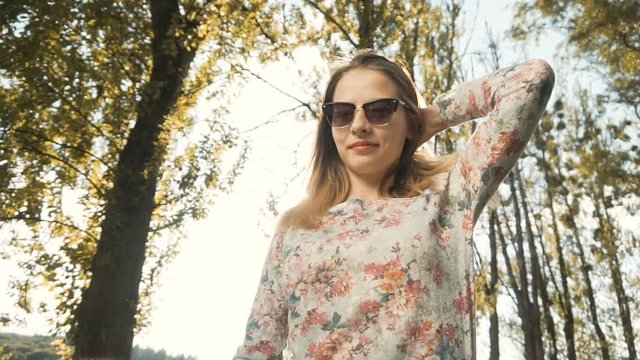 Portrait of cute hipster girl wears sunglasses in the park against sunset, 120FPS slowmotion