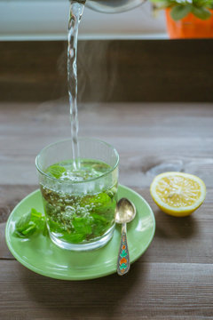 pouring hot water at the tea mug with mint and a lemon on a dark table