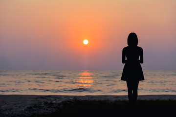 Fototapeta premium Silhouette of a woman standing by the sea and the sunset