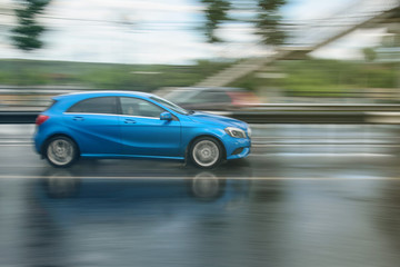 blue car driven on rainy roads with blur background