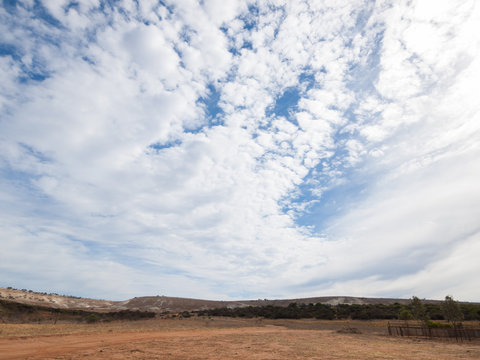 a wide angle shot of the harsh arid red landscape of the australian outback bush, with a cloudy  blue sky backdrop
