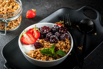 Healthy breakfast. Summer berries and fruits. Homemade Greek yogurt with granola, blackberries, strawberries and mint. On a black stone table, with the ingredients.