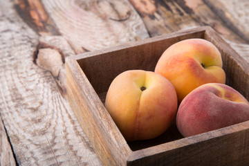 Three peaches in brown wooden box standing on rustic wooden background