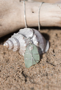 Unique handmade aqua marine sea glass jewellery, with a silver chain on a rustic sand and driftwood background