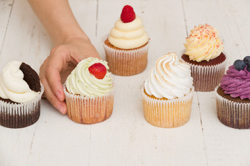Closeup of homemade vanilla, blueberyy, lemon, chocolate cupcakes and woman's  hand on white retro wooden background. Eating cupcake.Healthy food, snack for birthday party or celebration