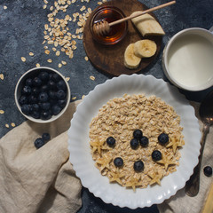 Organic oatmeal porridge with blueberry, banana, honey and milk on dark stone table, healthy lifestyle and diet concept, natural food, tasty breakfast, top view