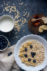 Organic oatmeal porridge with blueberry, banana, honey and milk on dark stone table, healthy lifestyle and diet concept, natural food, tasty breakfast, top view