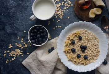 Organic oatmeal porridge with blueberry, banana, honey and milk on dark stone table, healthy lifestyle and diet concept, natural food, tasty breakfast, top view, space for text