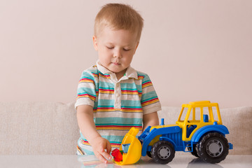 Portrait of cute toddler boy playing with colorful toy tractor. Child playing with a car at a nursery or preschool.