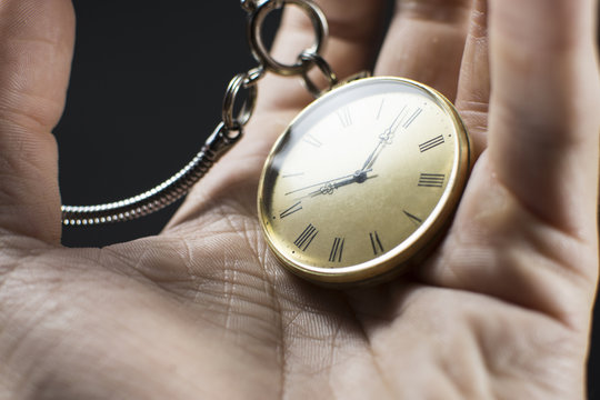 Close up of an old gold pocket watch in man's hand. Beautiful antique watch isolated on black background.