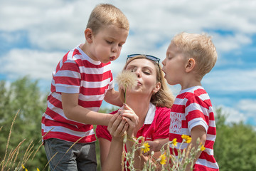 Mom and two young sons blow to the bouquet of dandelions.