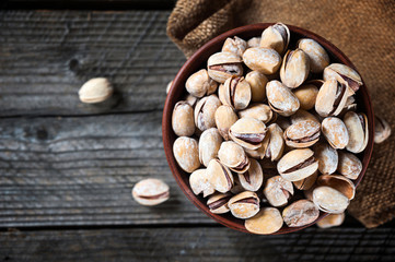 Salted roasted pistachios nuts in broun small bowl over old rustyc wooden textured background.
