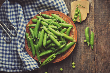 Young peas in a wooden plate on a wooden table. Standing next to a plate of pea pods.