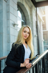 Smiling beautiful young girl with blond hair in a black suit, in the courtyard of a modern building