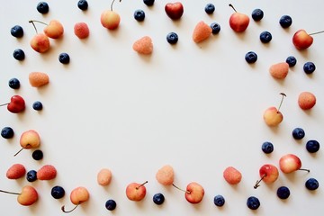 A lot of fresh, organic and tasty fruits (blue blueberry, cherry, gold raspberry) on the white table