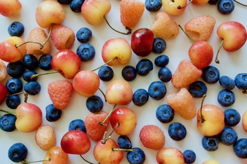 A lot of fresh, organic and tasty fruits (blue blueberry, cherry, gold raspberry) on the white table
