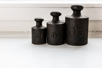 Antike Gewichte aus Metall für alte Waagen, auf einem weißen Holzfensterbrett