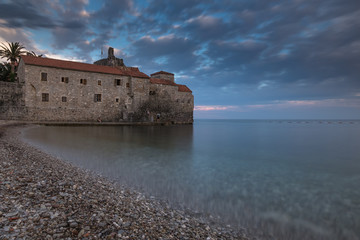 Ancient town on the edge of the sea with blurred water surface and colorful dramatic sky at sunset