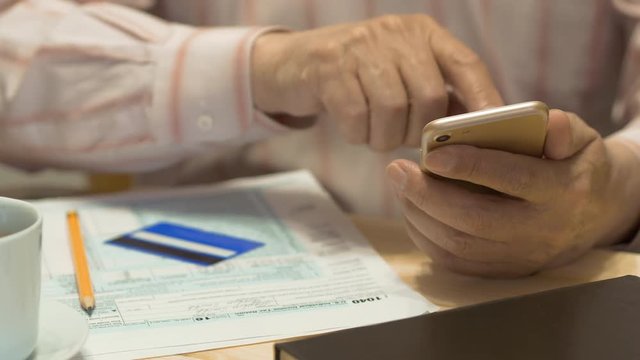 Elderly Man Text Messaging On Smartphone And Tax Form 1040