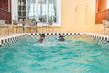 Fototapeta premium Two little girls swimming in swimming pool,they children so happy,bright sunlight,sunny day,from back