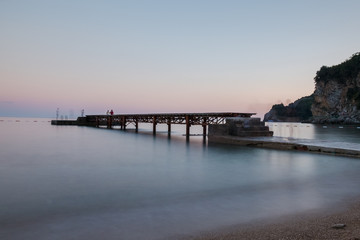 Wooden dock at the beach with blurred water at sunset and people silhouettes 