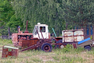 старый ржавый трактор с прицепом и металлоломом в поле возле деревьев