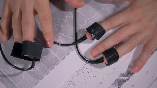 Hands with finger sensors lying above polygraph printouts. 4K 60 fps.