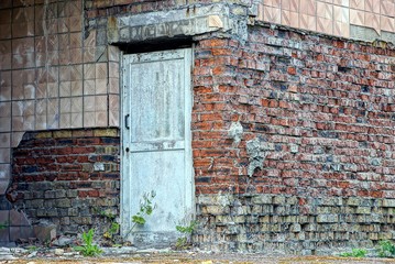Старая серая дверь на стене заброшенного кирпичного дома
