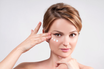 Naklejka premium Beauty and skincare concept. Young woman applying moisturizer on face.