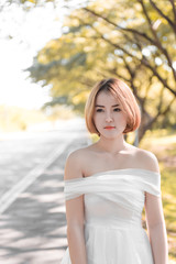 Fototapeta na wymiar Beautiful thai woman in white dress gold hairs stand on the road under tunnel tree in the sunny day,bright sunlight
