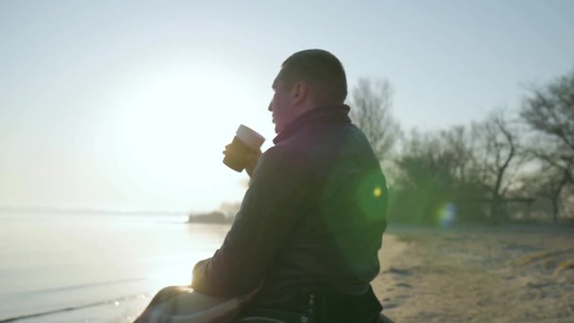 disabled close-up drinks coffee, portrait lonely male cripple on wheelchair, outdoors, handicapped on nature, embankment along sea, invalid on wheel chair, faith in future, slow motion