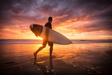 Surfer running on the beach ar sunset or sunrise