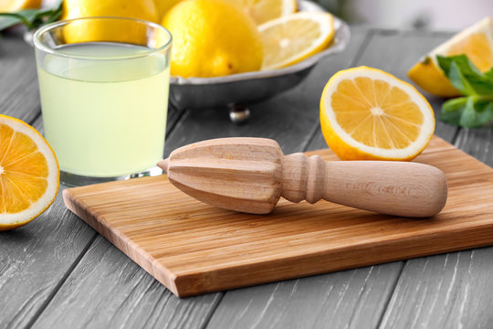 Cutting board with juicer, glass of juice and lemon on wooden table
