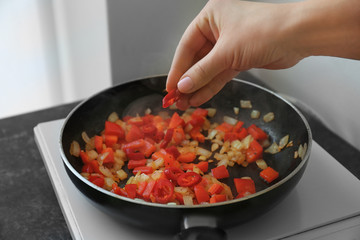 Female hand putting chili pepper into frying pan