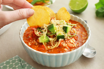 Female hand putting chips into bowl with chili turkey, closeup
