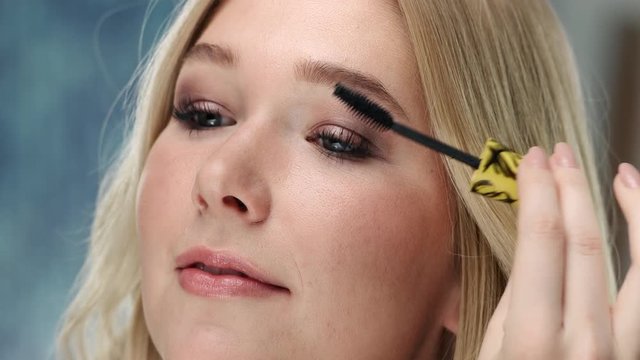 Young caucasian woman is applying mascara at her eyelashes