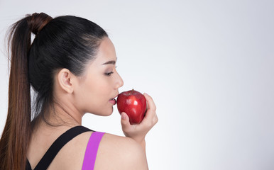 asian healthy athletic sporty girl with red apple after training. attractive smiling woman standing against white background.