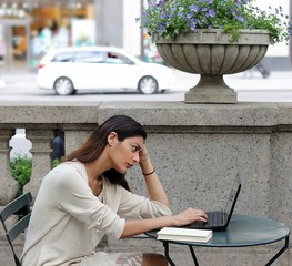 Young attractive woman sitting outside in urban park fustrated studying