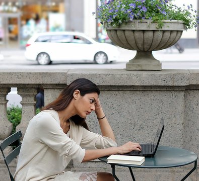 Young attractive woman sitting outside in urban park fustrated studying